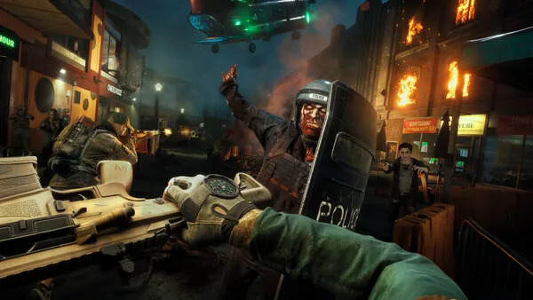 Official No More Room in Hell 2 screenshot showing a firearm used against a riot-shield zombie in a burning city street